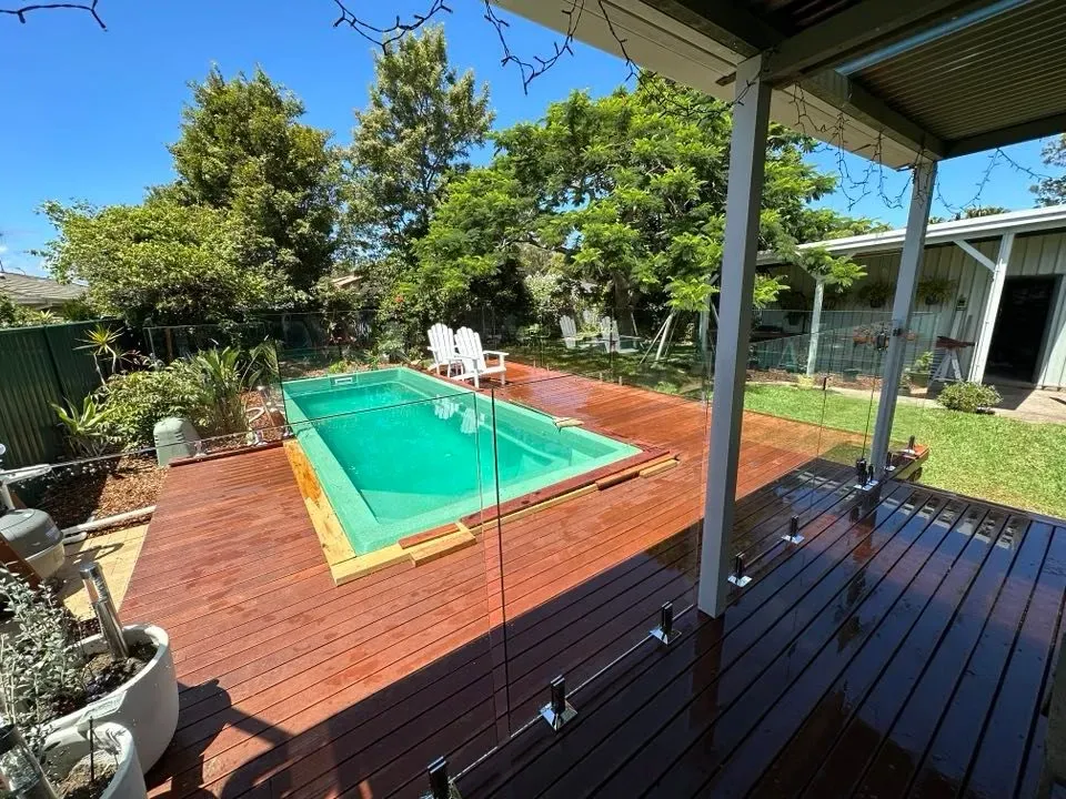 A large swimming pool is surrounded by a glass fence and a wooden deck — Mid Coast Glass Fencing In Forster, NSW