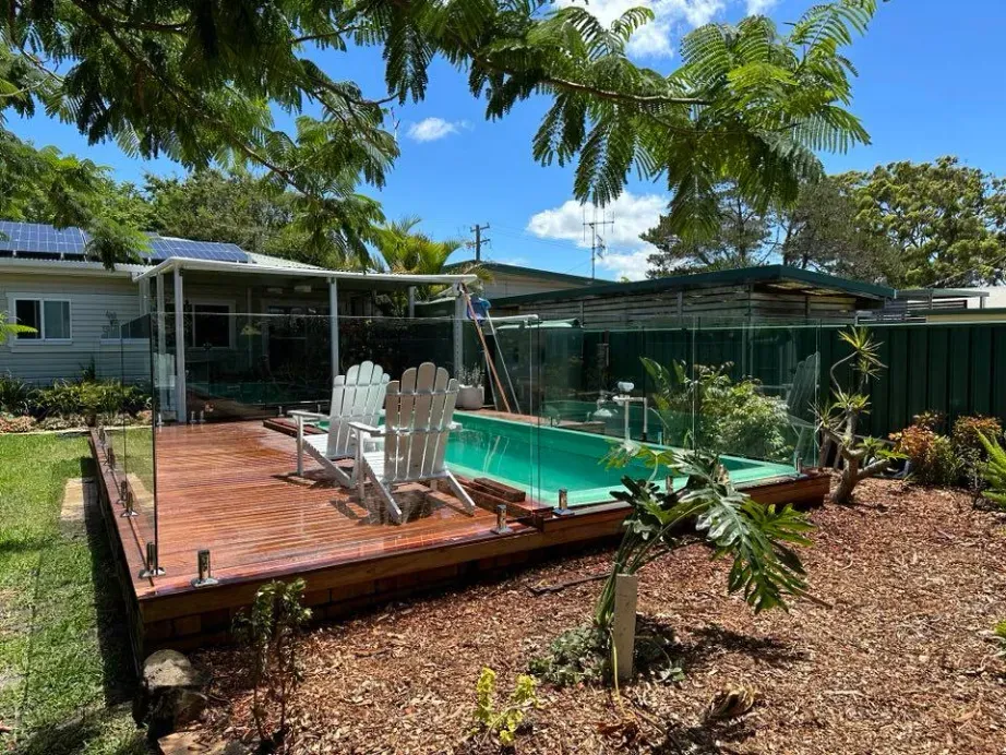 A Swimming Pool Is Surrounded By A Glass Fence And A Wooden DECK — Mid Coast Glass Fencing In Port Macquarie, NSW