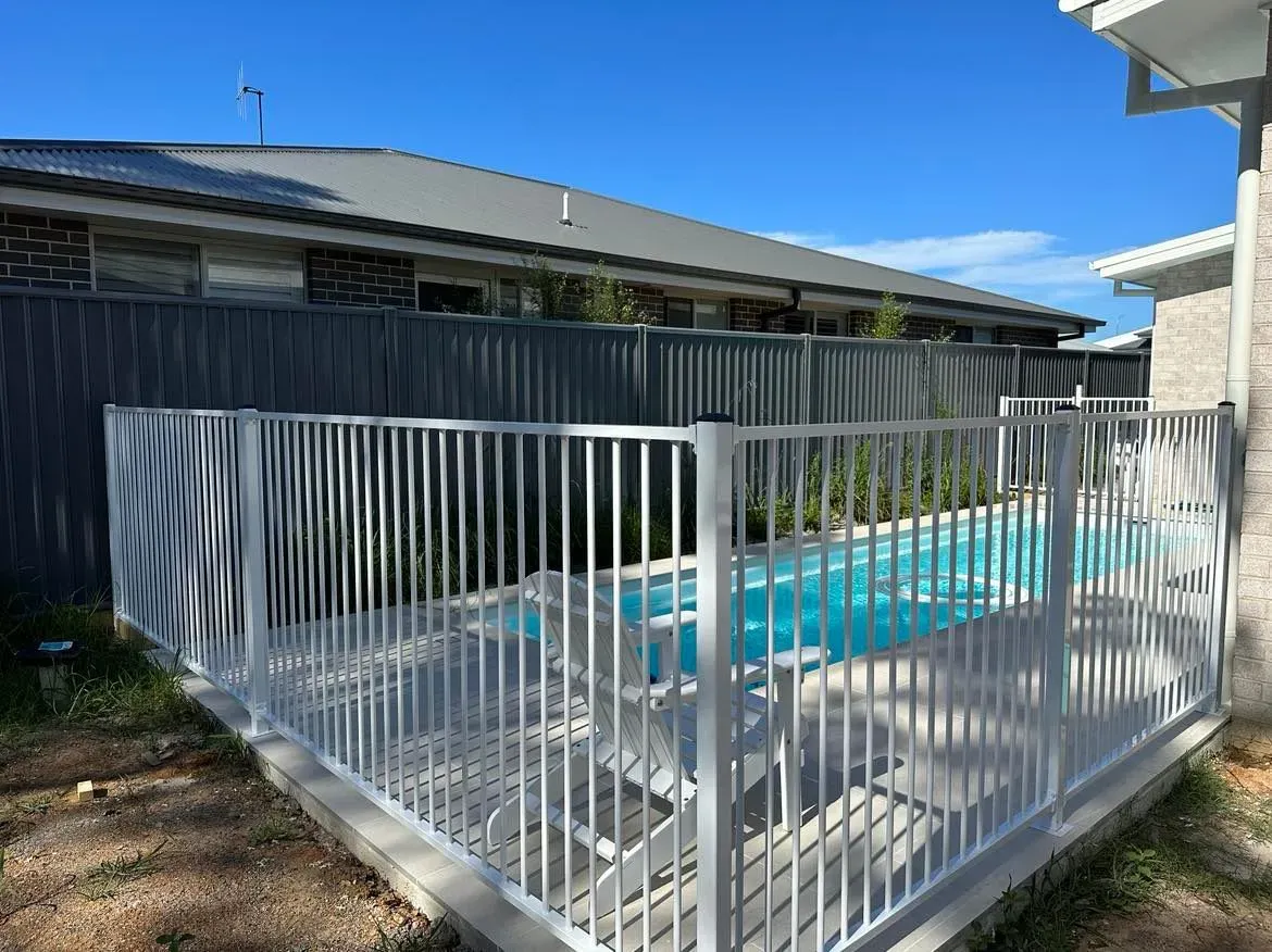 A White Fence Surrounds A Swimming Pool In The Backyard Of A HoUSE — Mid Coast Glass Fencing In Wauchope, NSW