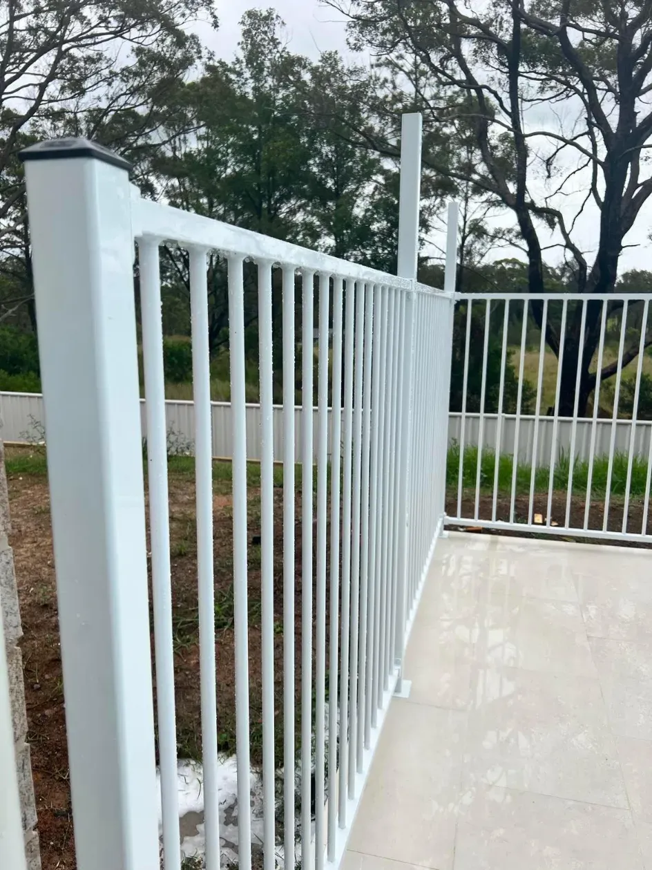 A close up of a white fence with trees in the background — Mid Coast Glass Fencing In Wauchope, NSW