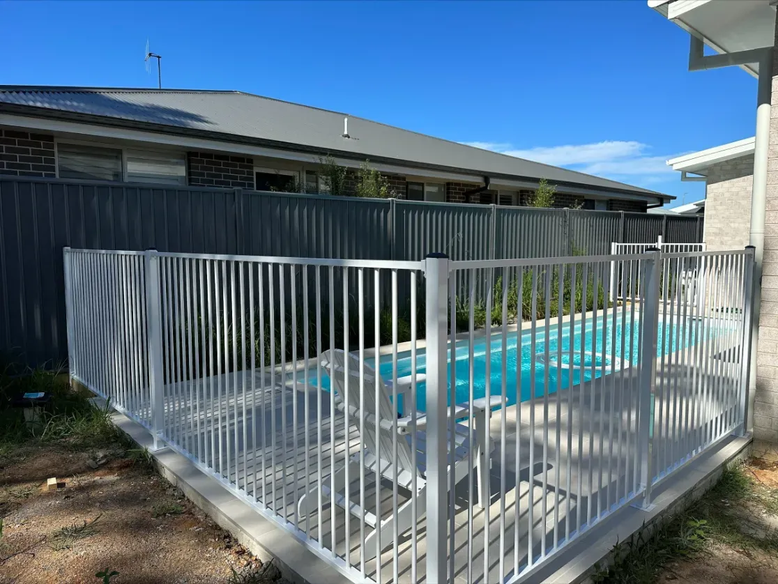 A white fence surrounds a swimming pool in a backyard — Mid Coast Glass Fencing In Wauchope, NSW