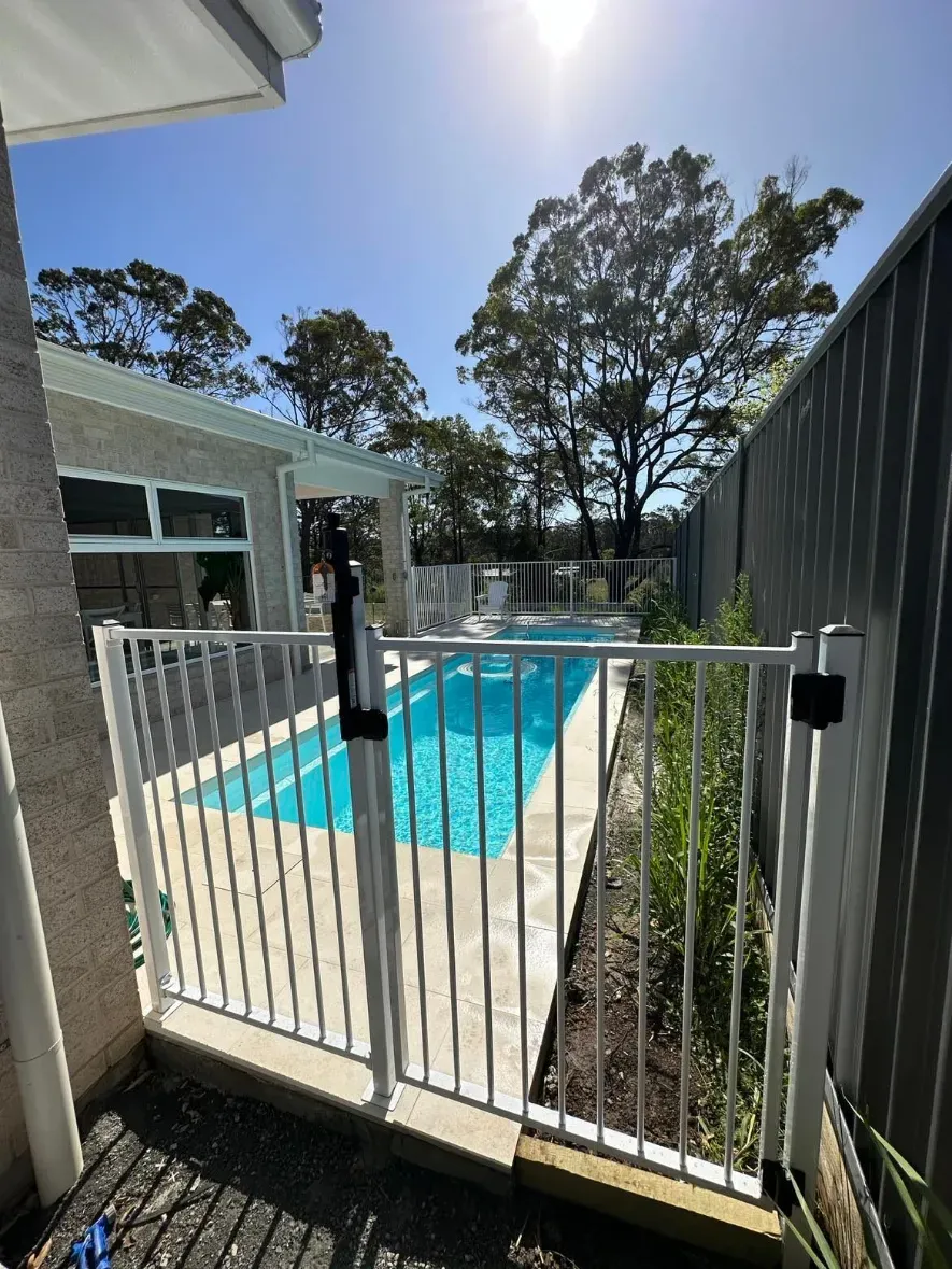 A white gate leading to a swimming pool with a house in the background — Mid Coast Glass Fencing In Wauchope, NSW