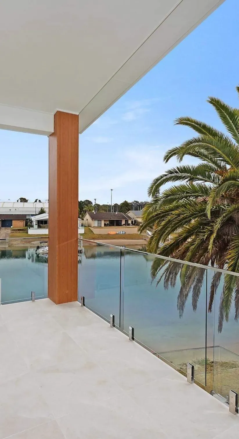 A Balcony Overlooking A Body Of Water With A Palm Tree In The BackgroUND — Mid Coast Glass Fencing In South West Rocks, NSW
