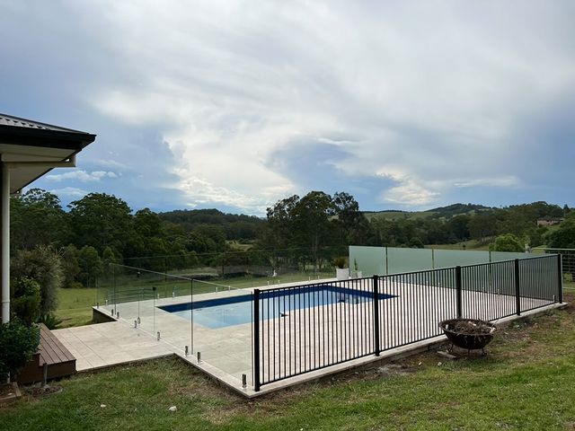 A Large Swimming Pool Surrounded By A Fence And A House — Mid Coast Glass Fencing In Old Bar, NSW