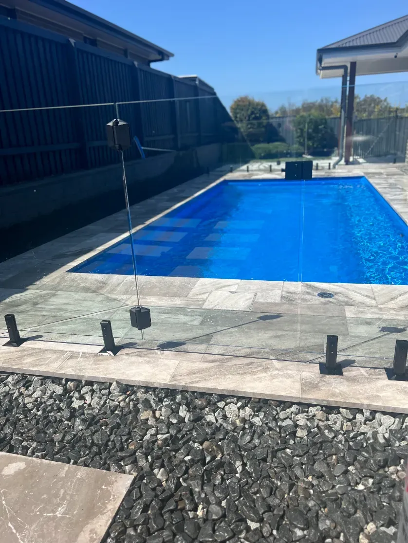 A large blue swimming pool with a glass fence around it — Mid Coast Glass Fencing In Forster, NSW