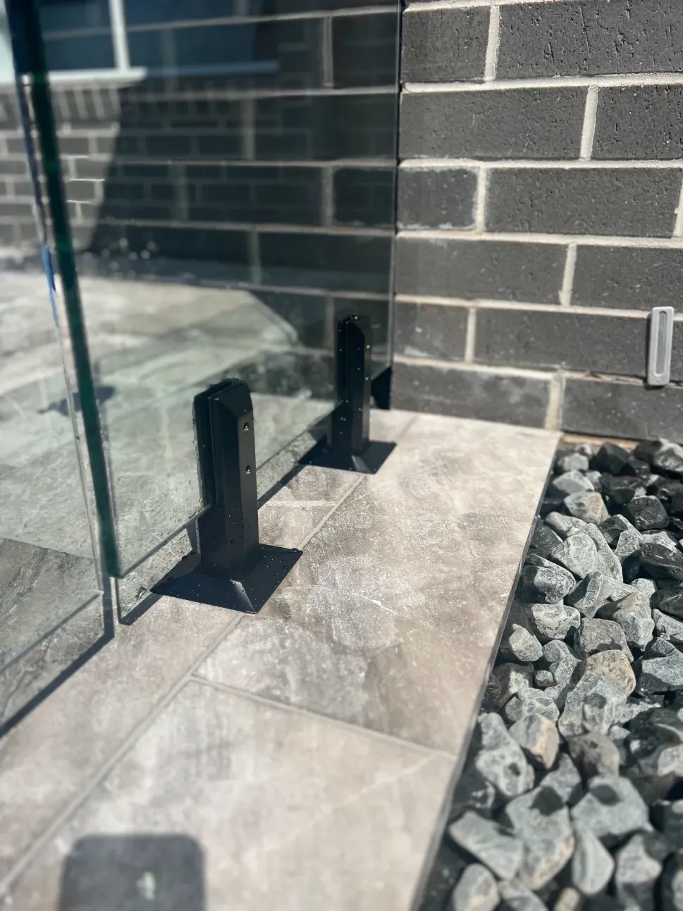 A glass railing is sitting on a tiled floor next to a brick wall — Mid Coast Glass Fencing In Forster, NSW