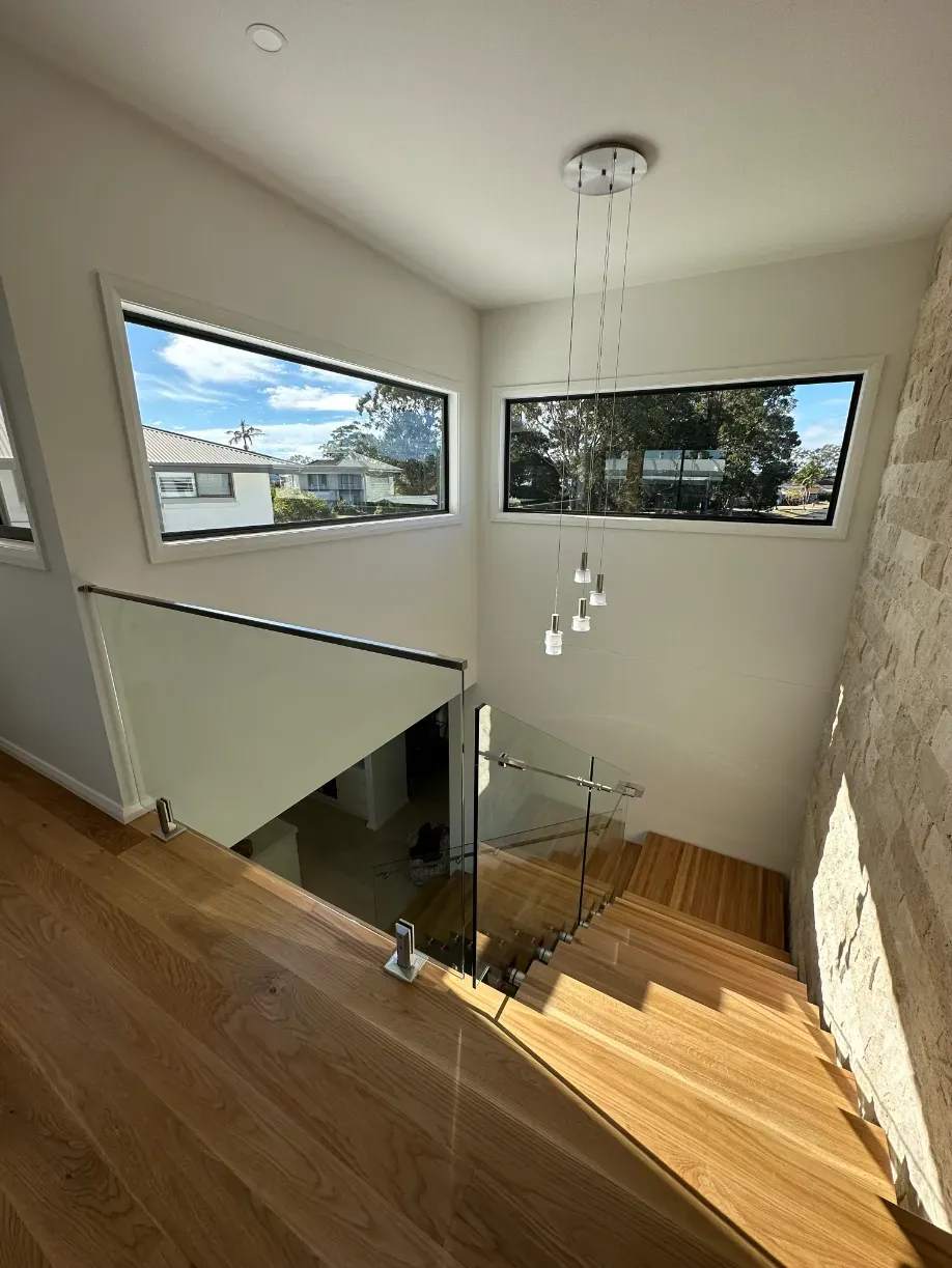 A staircase with a glass railing and a large window — Mid Coast Glass Fencing In Taree, NSW