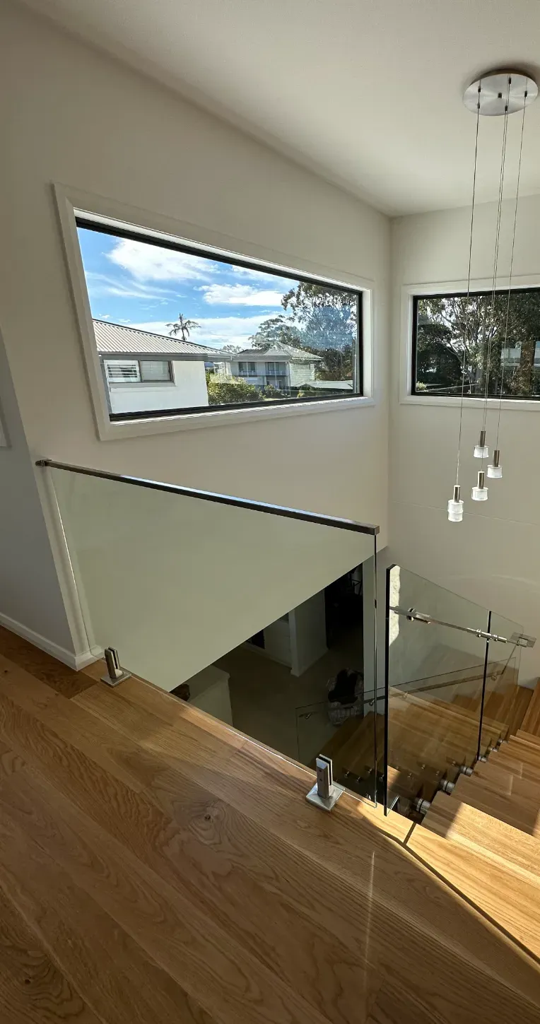 A staircase with a glass railing and a large window — Mid Coast Glass Fencing In Taree, NSW
