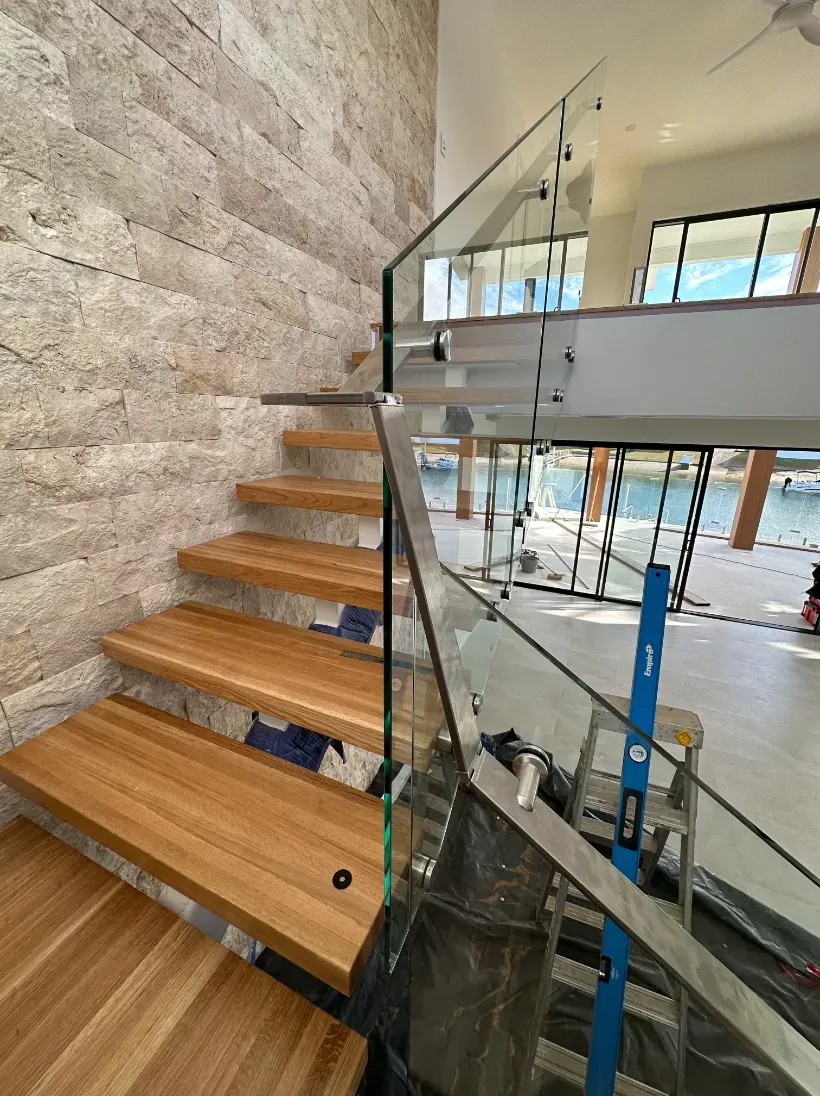 A Wooden Staircase With A Glass Railing In A HoUSE — Mid Coast Glass Fencing In Port Macquarie, NSW