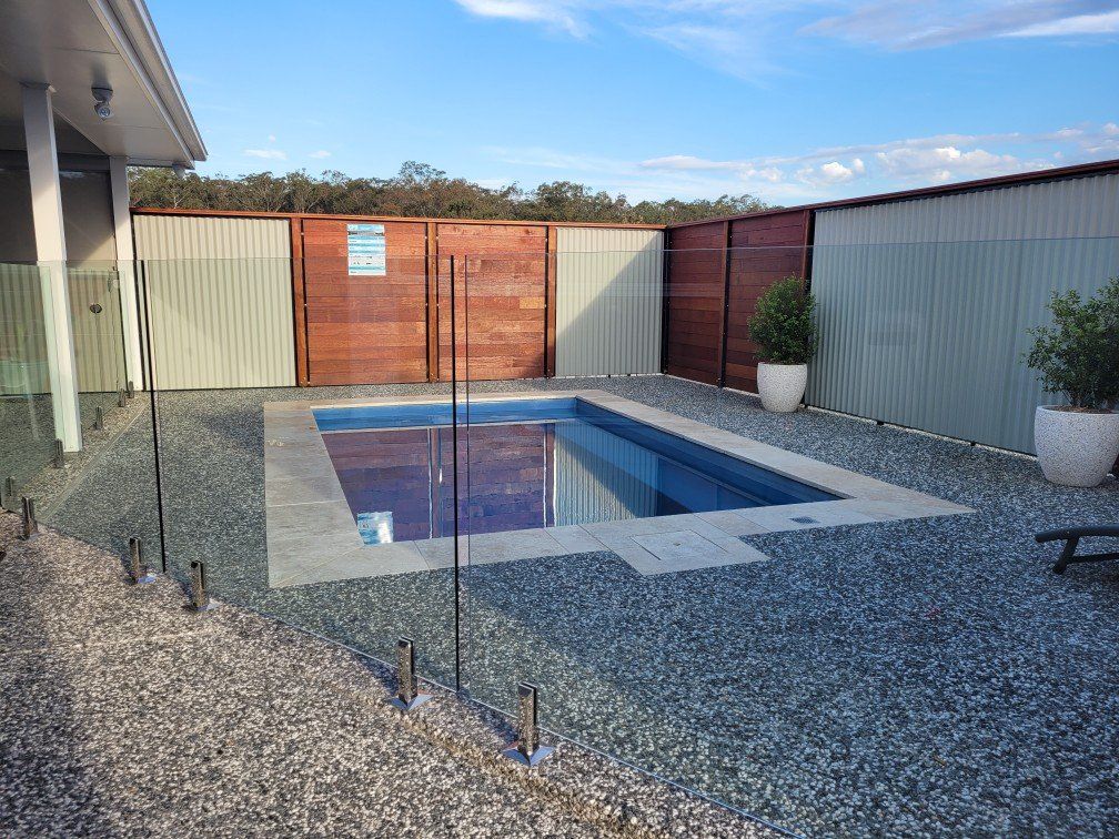 A large swimming pool is surrounded by a fence and gravel — Mid Coast Glass Fencing In Old Bar, NSW
