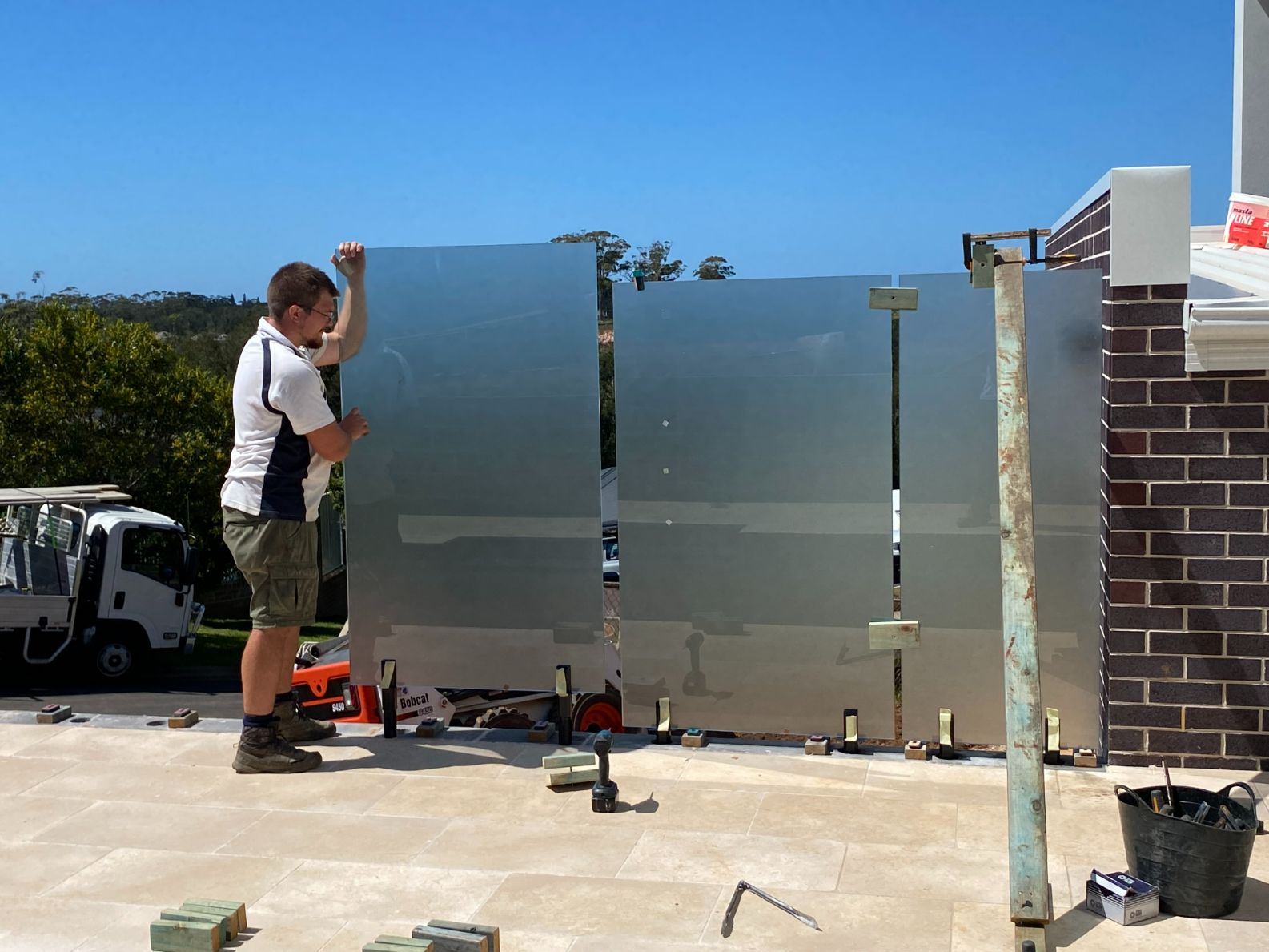 A man is working on a fence with a truck in the background — Mid Coast Glass Fencing In Old Bar, NSW