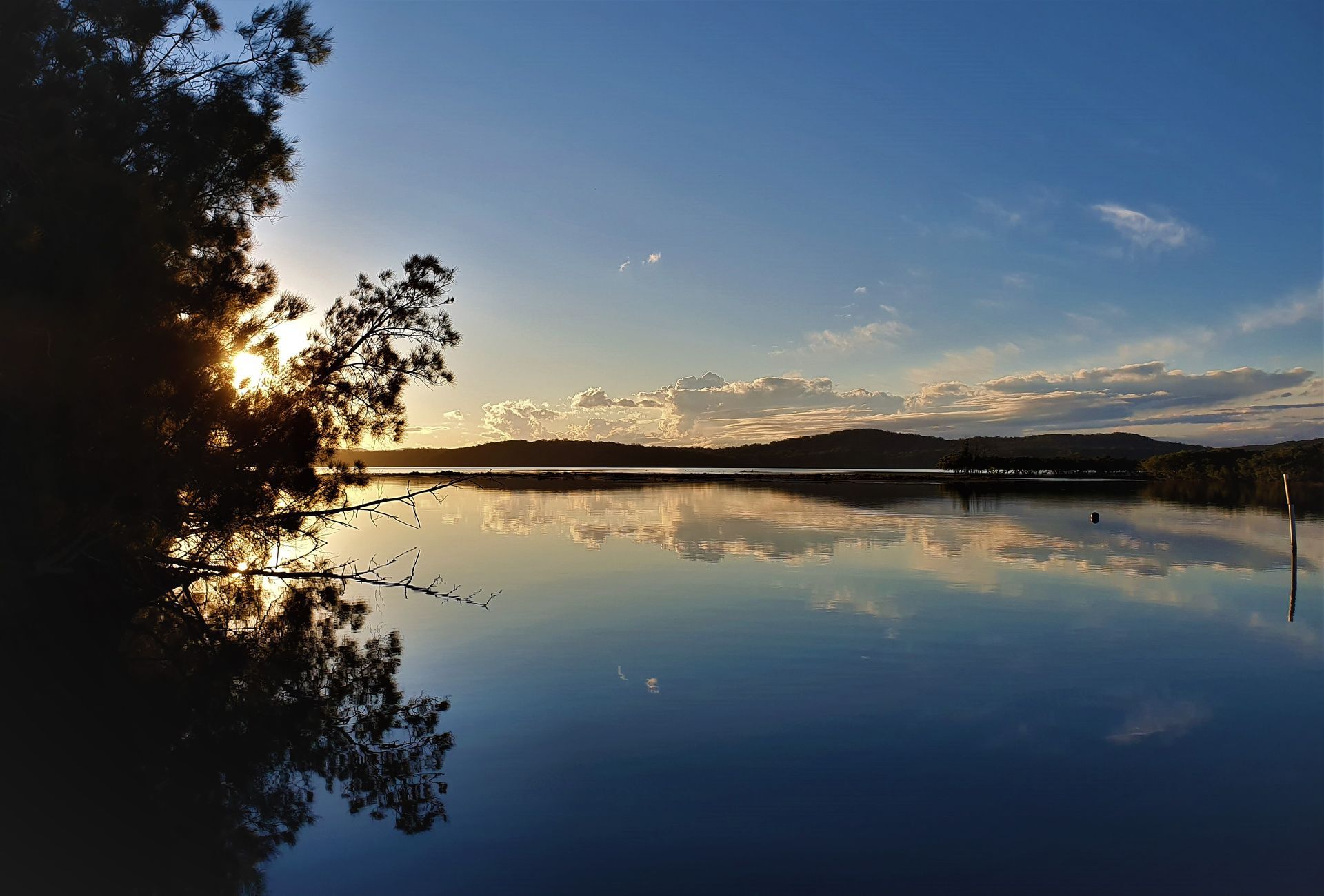 The sun is setting over a lake with trees in the foreground — Mid Coast Glass Fencing In Laurieton, NSW