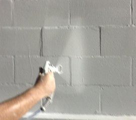 Learn more about our waterproofing service A person is spraying white paint on a brick wall .