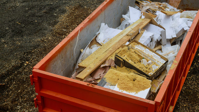 Orange dumpster filled with construction debris, including wood and insulation.