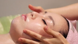 A woman is getting a facial massage with her eyes closed