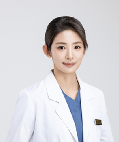 A woman in a white coat and blue scrubs is smiling for the camera.