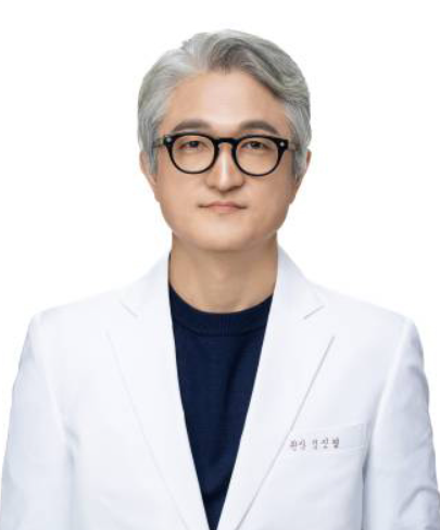 A man wearing glasses and a white coat is standing in front of a white background.