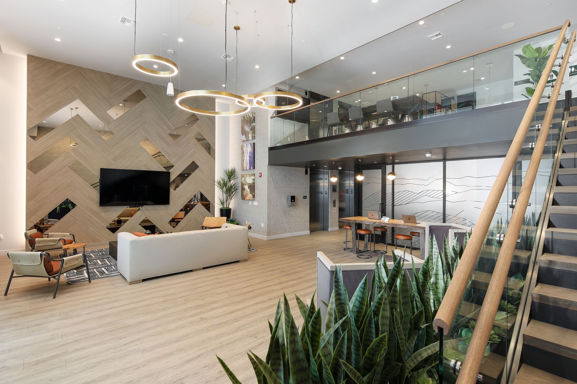 Modern hotel lobby with high ceilings, white seating, hanging ring lights, staircase, and indoor plants