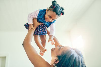 Adult lifting smiling child overhead indoors, both reaching toward each other