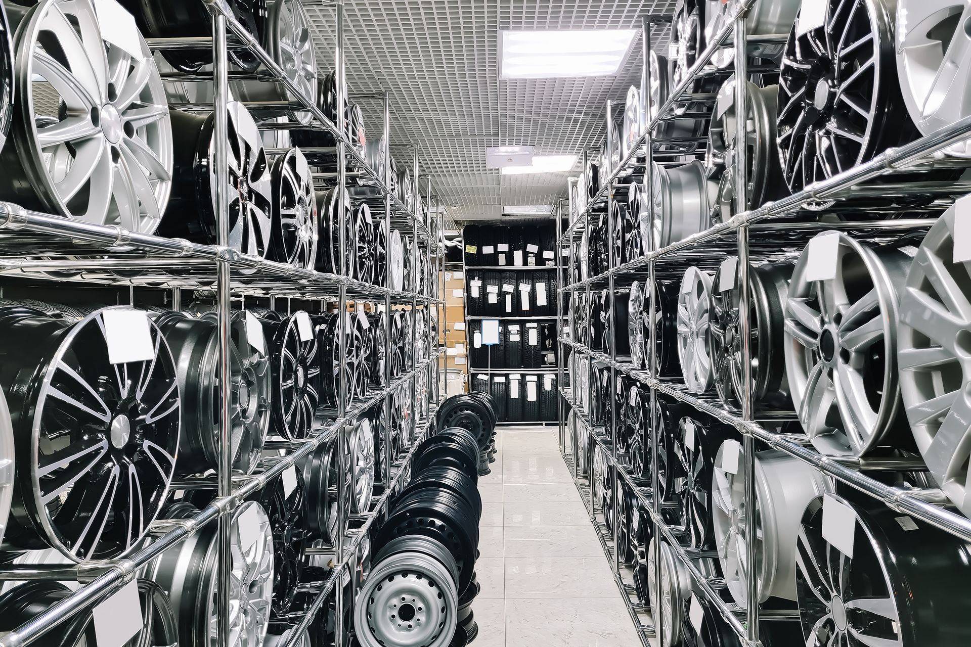 Warehouse storage of car rims and wheels on metal shelves, organized in rows. 