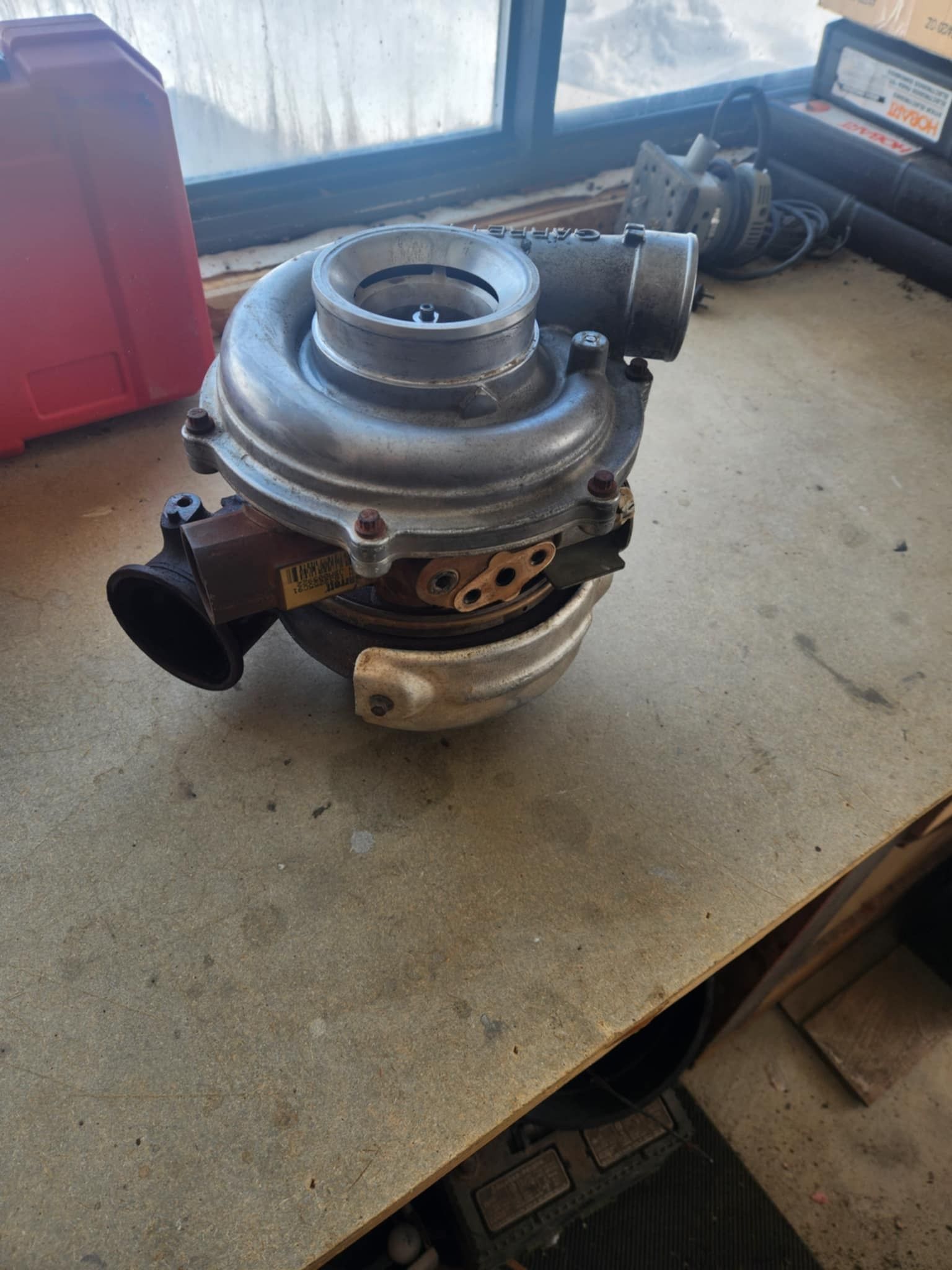A silver turbocharger on a concrete surface with a rusty exhaust port.