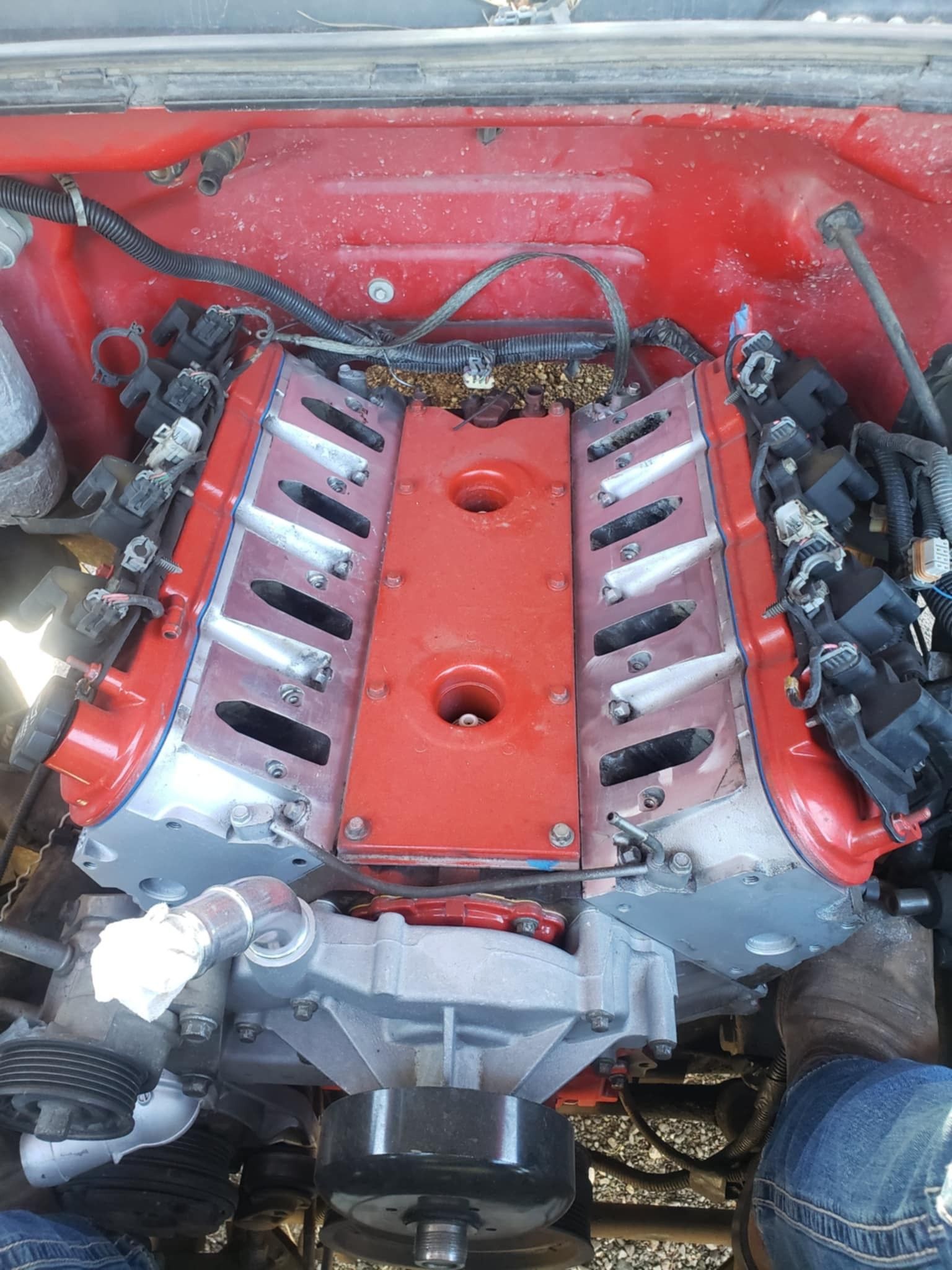 Red engine in a car, viewed from above. The engine is partially disassembled, showing silver and red components.