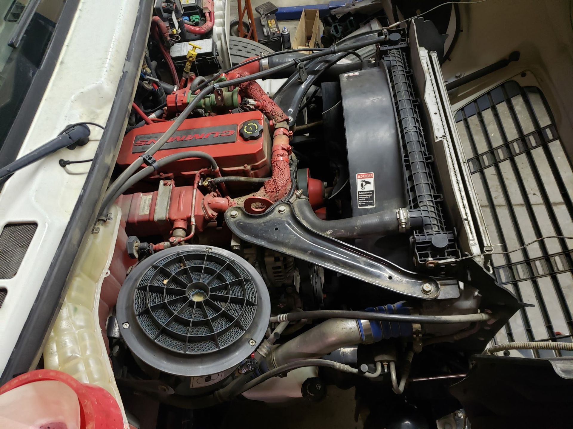 Open engine compartment of a white truck, showing the red engine components, radiator, and large fan.