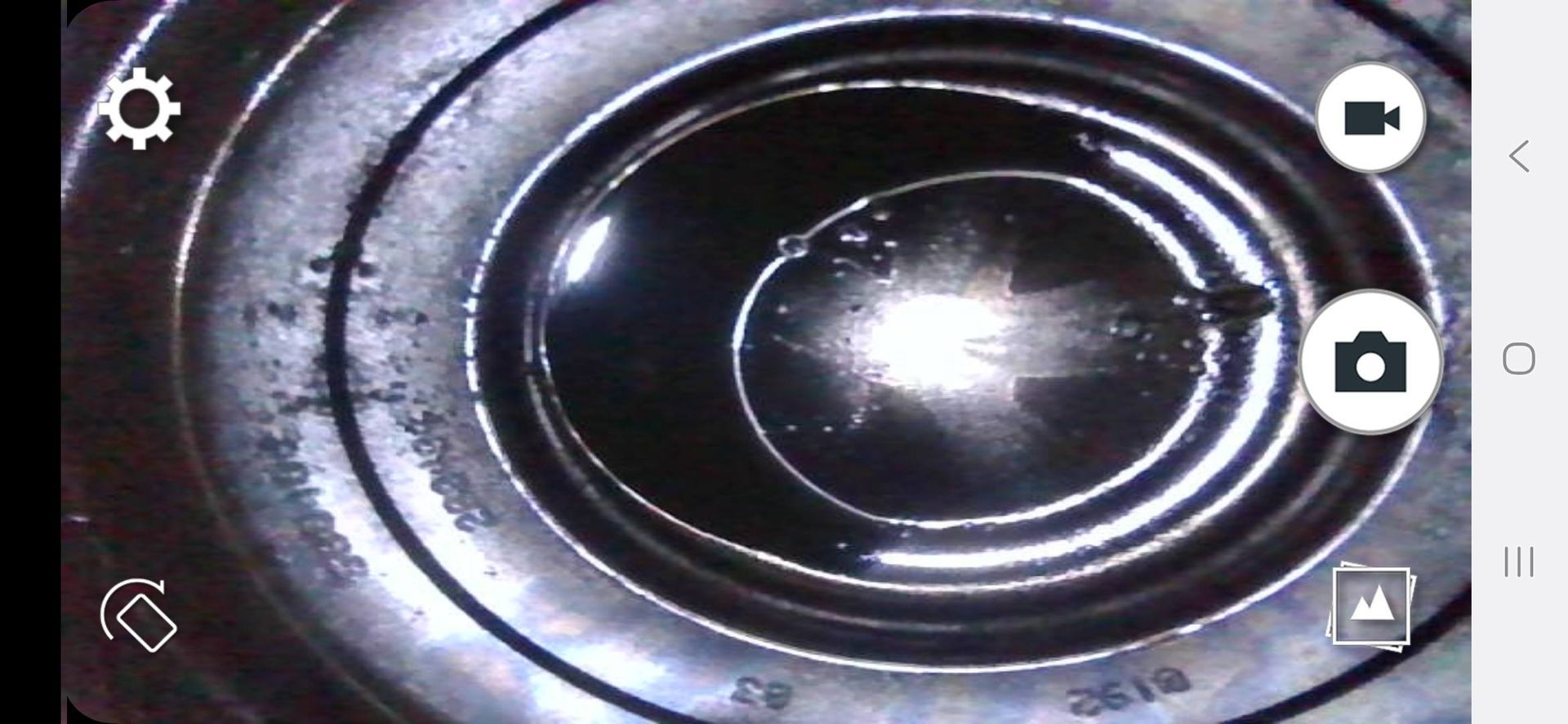 An inside view of a metal component with concentric circles. A light source reflects in the center, surrounded by a dark, liquid-like substance.