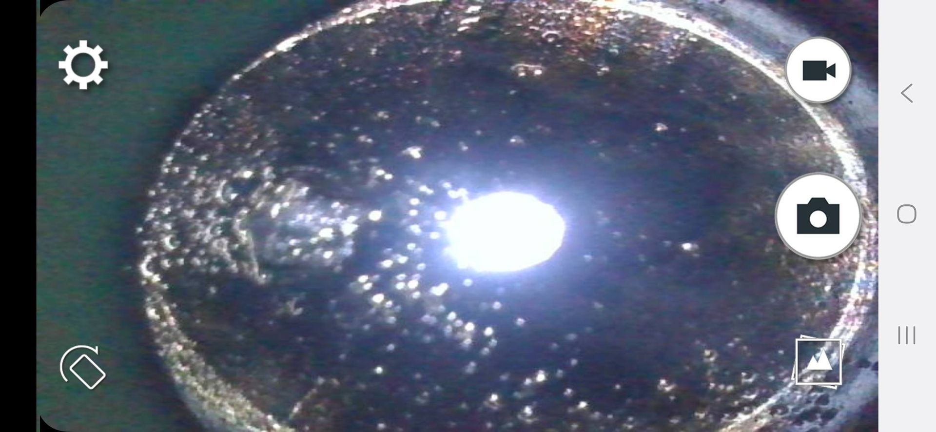 A close-up shot inside a dark tube with a bright, glowing center. Small, uneven objects are visible around the edge.