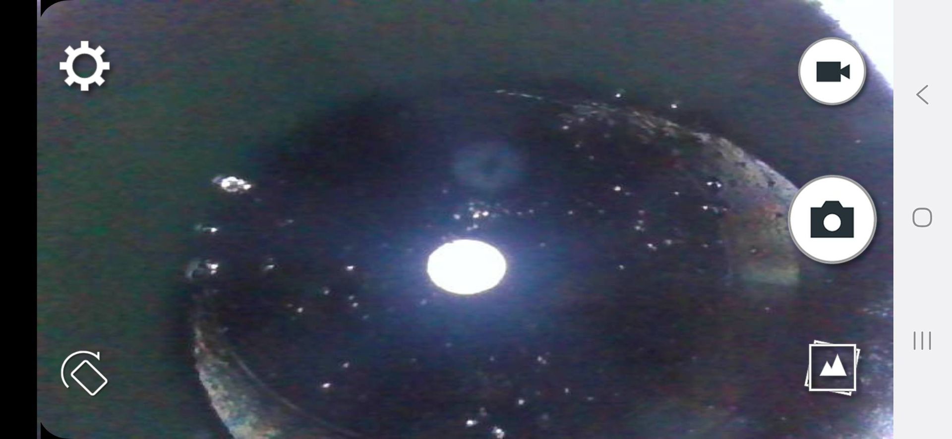 View from inside a dark hole with a bright light in the center. The camera app interface is visible.
