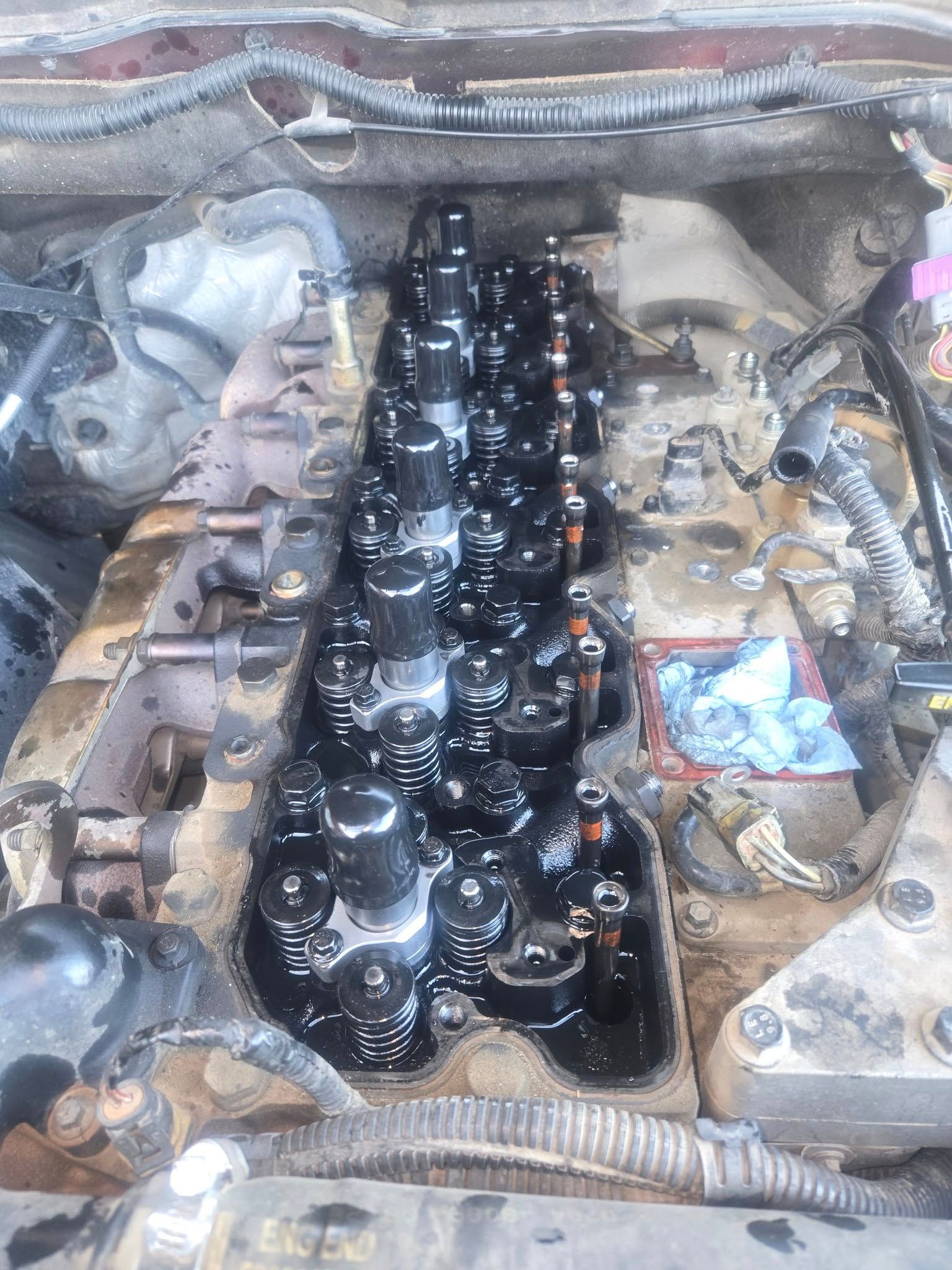 Engine cylinder head with black oil covering the components, viewed from above.