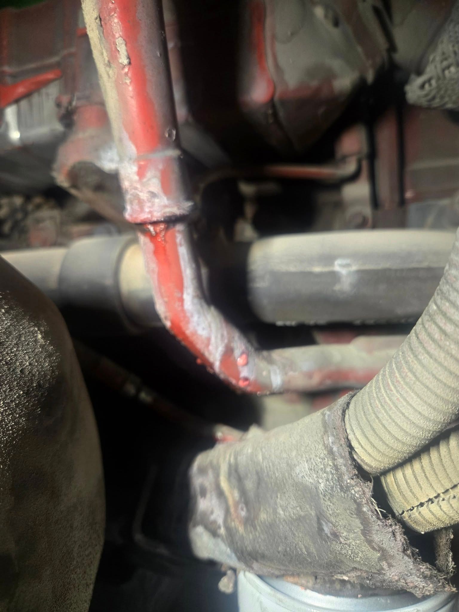 Red-painted metal pipe with visible coolant leaking onto other components within an engine compartment.