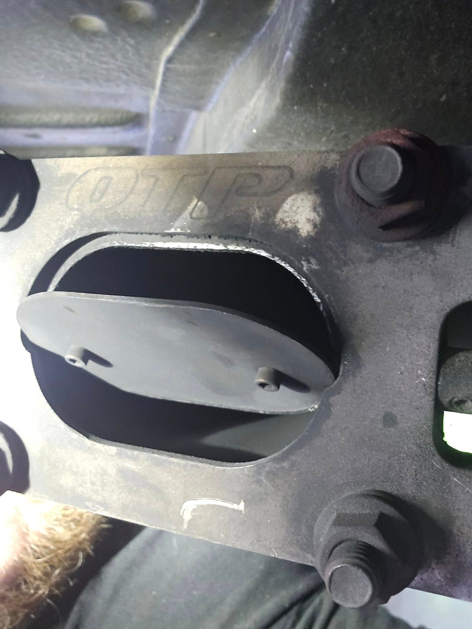 Close-up of a car exhaust component, showing a metal plate with a cut-out section. A flap is inside the cut-out.