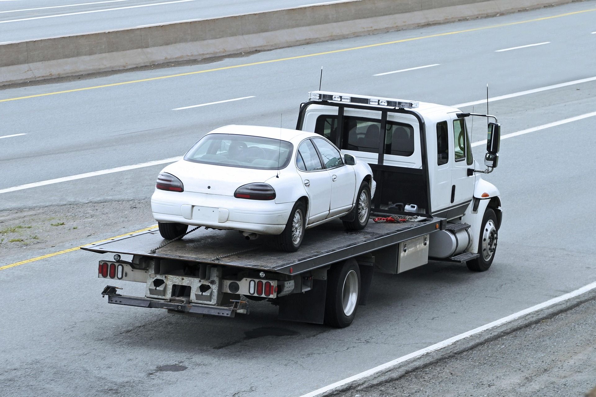 Tow truck carrying a white sedan on a highway shoulder