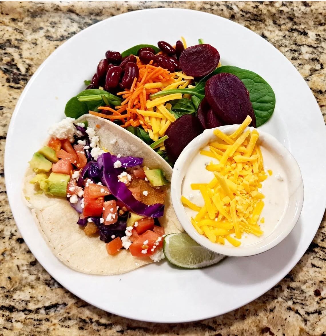 Taco on a white plate with salad, dip, and lime wedge.