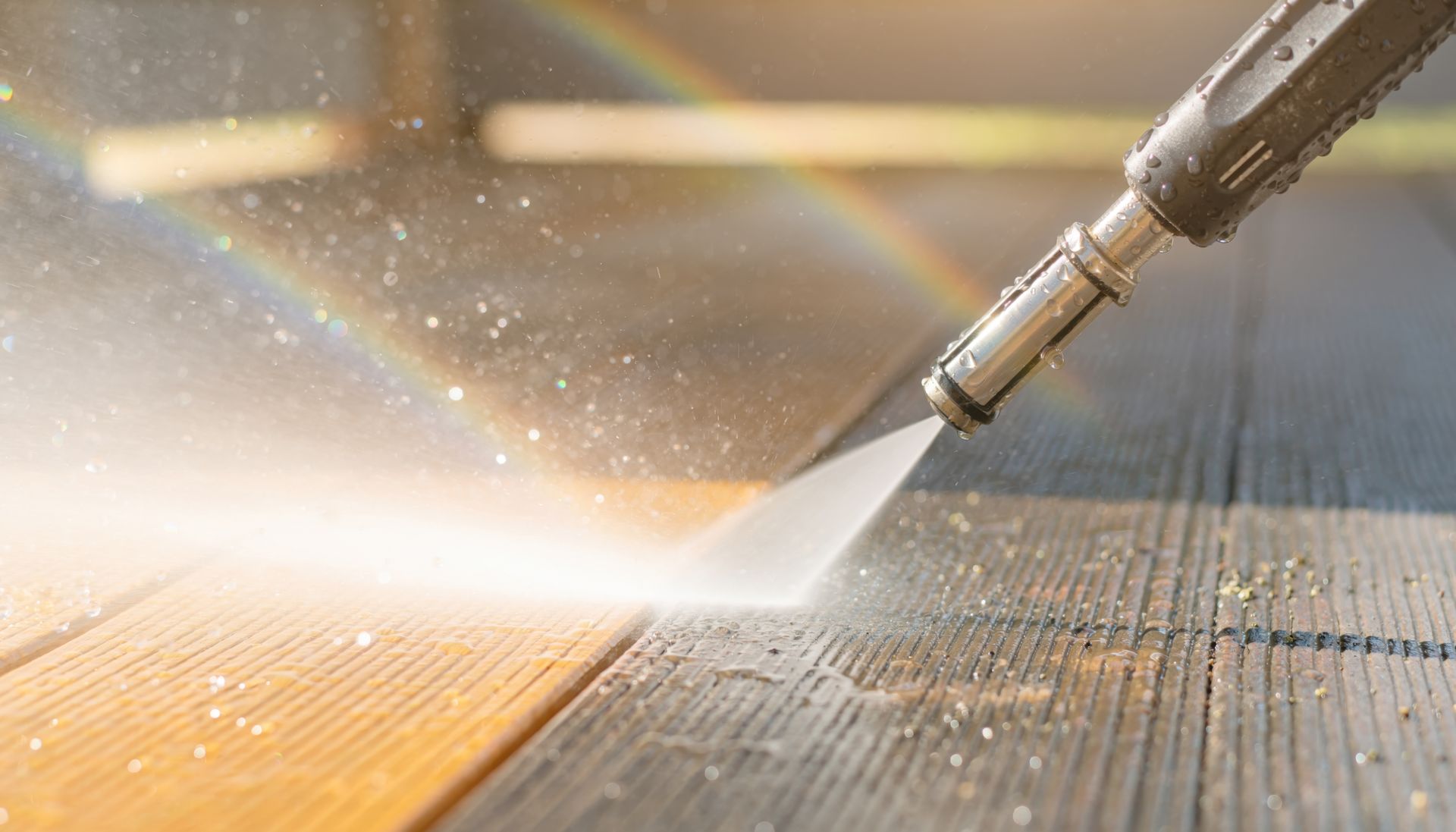 A pressure washer cleans dark, weathered wooden deck boards, revealing a bright, clean, lighter wood surface underneath.
