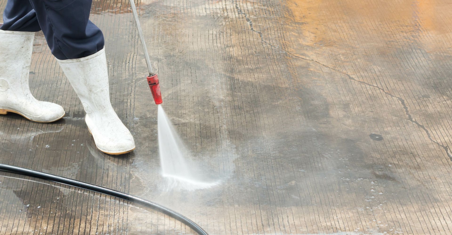 Person in white boots power washing a concrete surface.