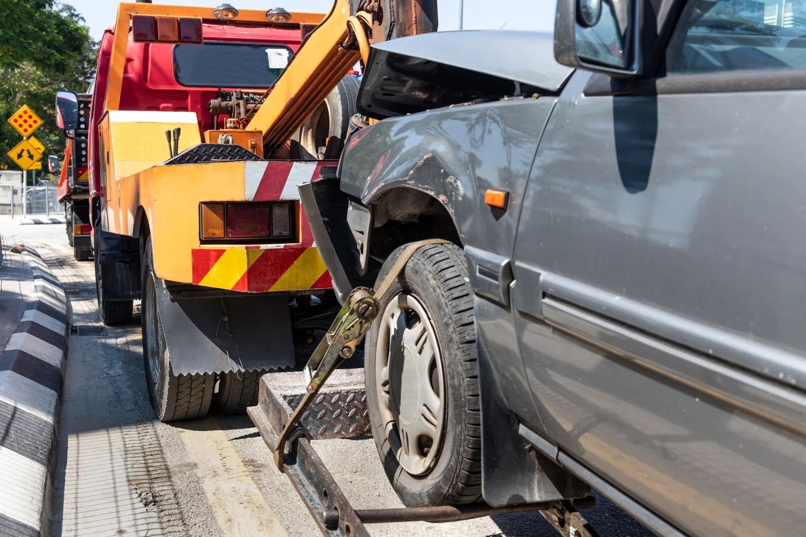 Tow truck loading a damaged gray car on a city street.