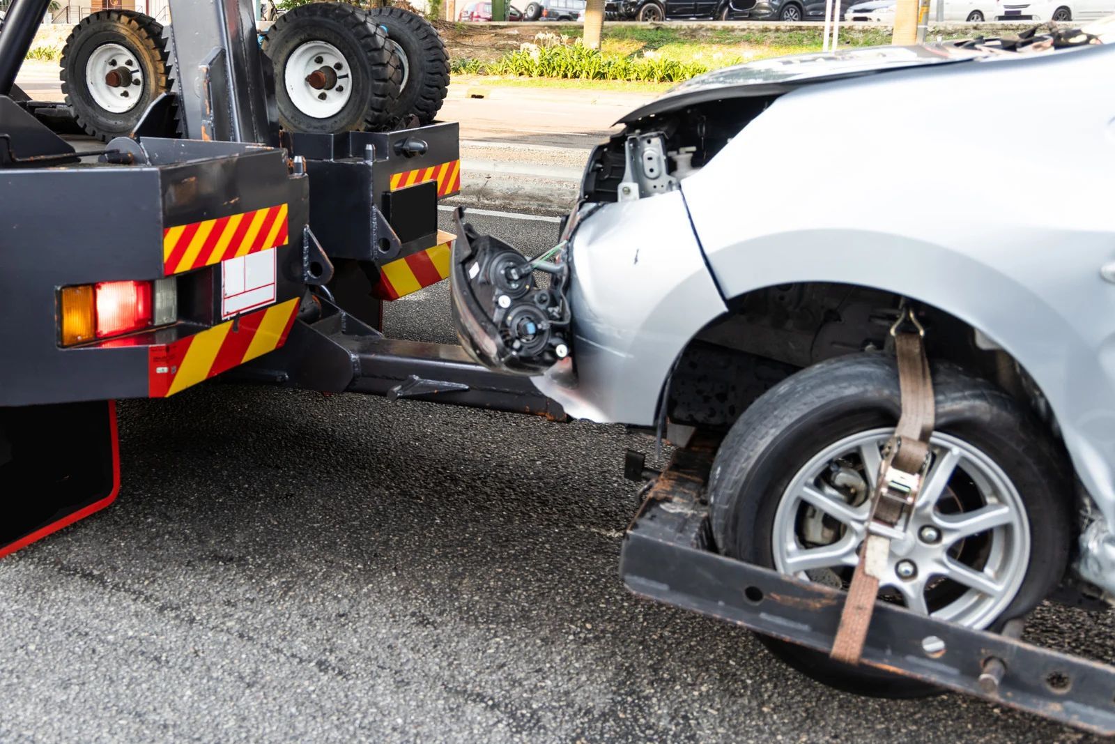 Damaged silver car being towed by a tow truck; front end severely damaged.