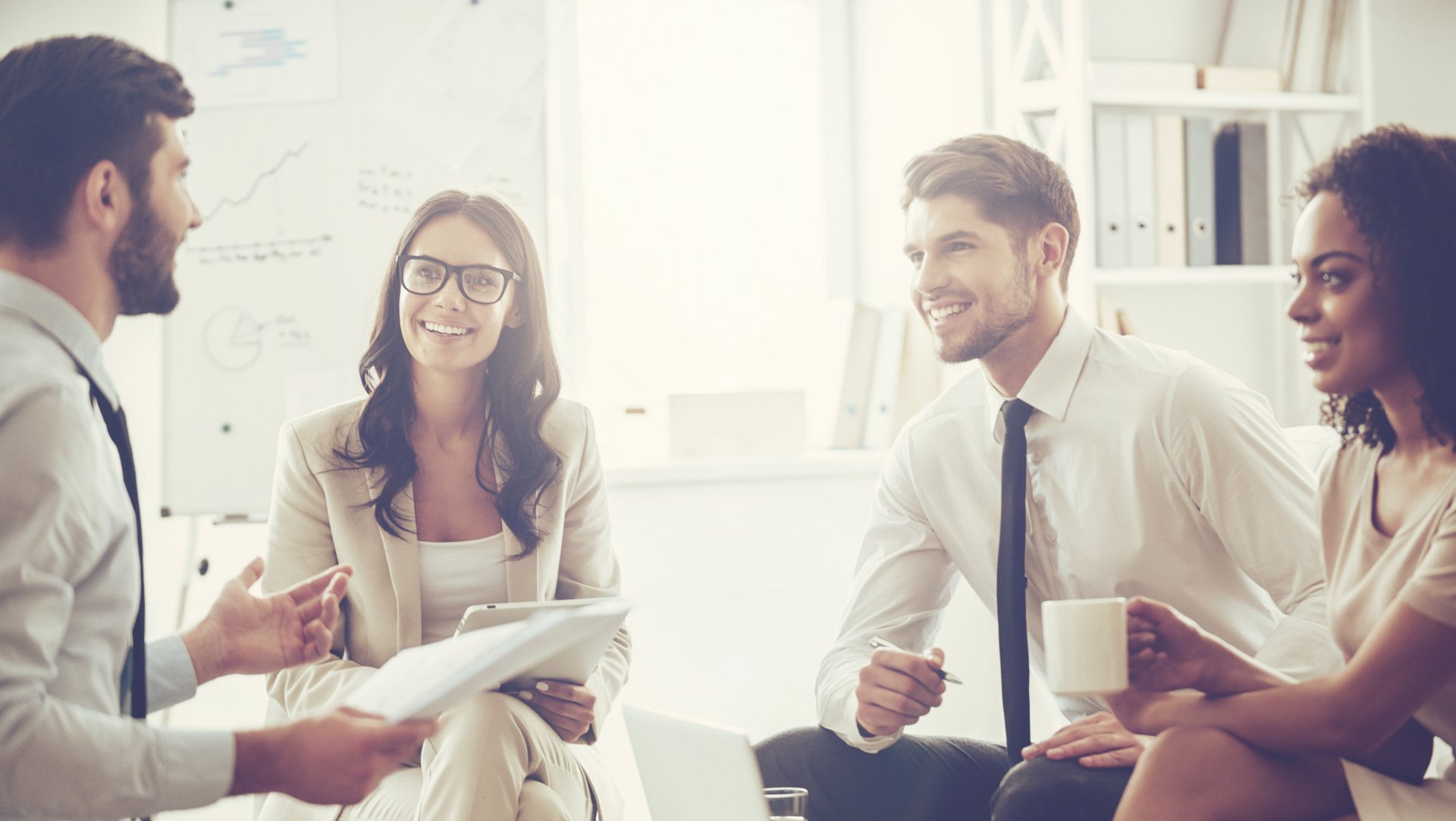 Our work is amazing! Young handsome man holding documents and discussing something with his coworkers with smile while sitting on the couch at office