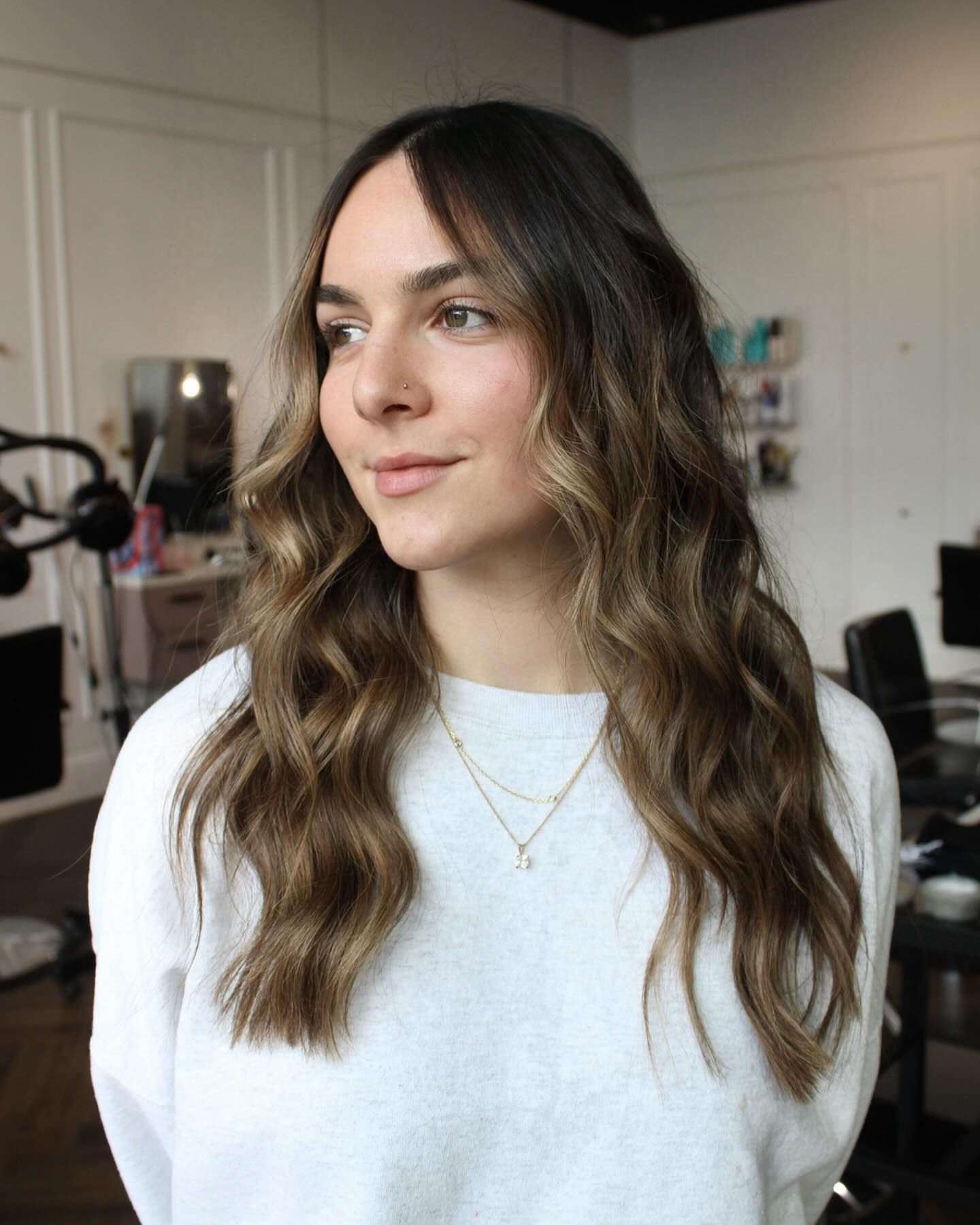 a woman with long brown hair is wearing a white sweater and a gold necklace .