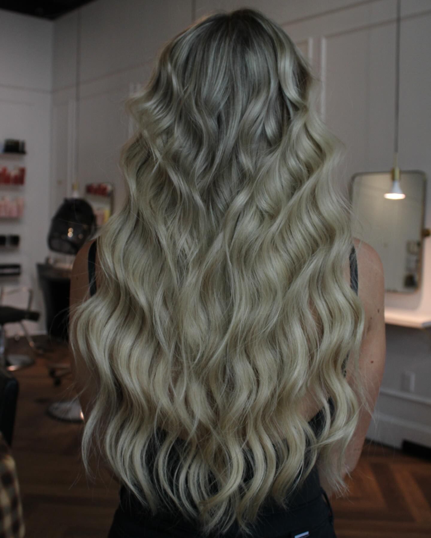 a woman with long blonde wavy hair is standing in a salon .