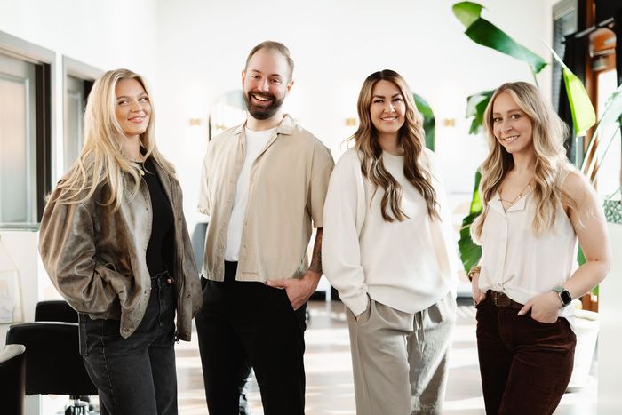 a woman wearing a white shirt and black jeans stands in front of a pink wall