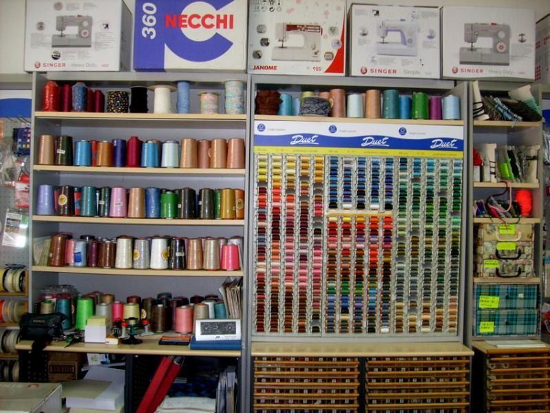 Scaffali di articoli per cucire: rocchetti di filo di vari colori, macchine da cucire e accessori in un negozio di tessuti.