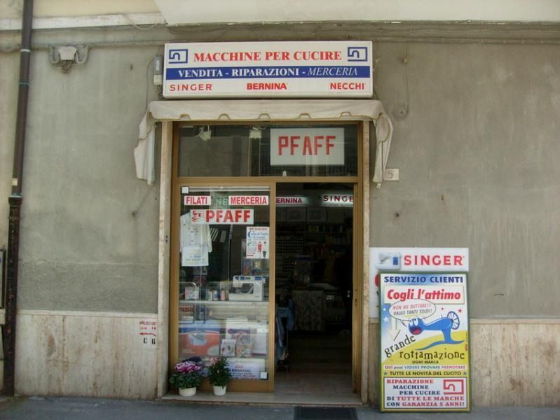 Esterno di un negozio di macchine da cucire con insegne per Singer, Pfaff e altri marchi.