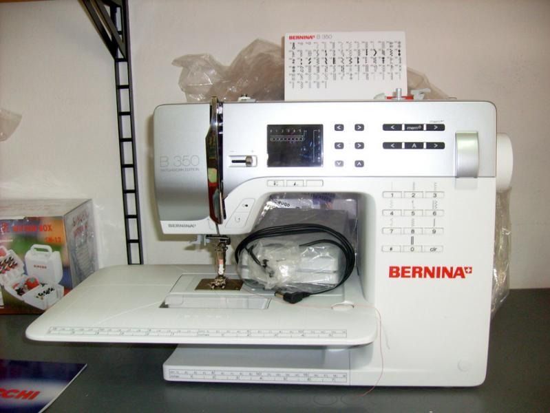 Macchina da cucire Bernina bianca su un tavolo con accessori, un pannello di controllo e un piccolo calendario.