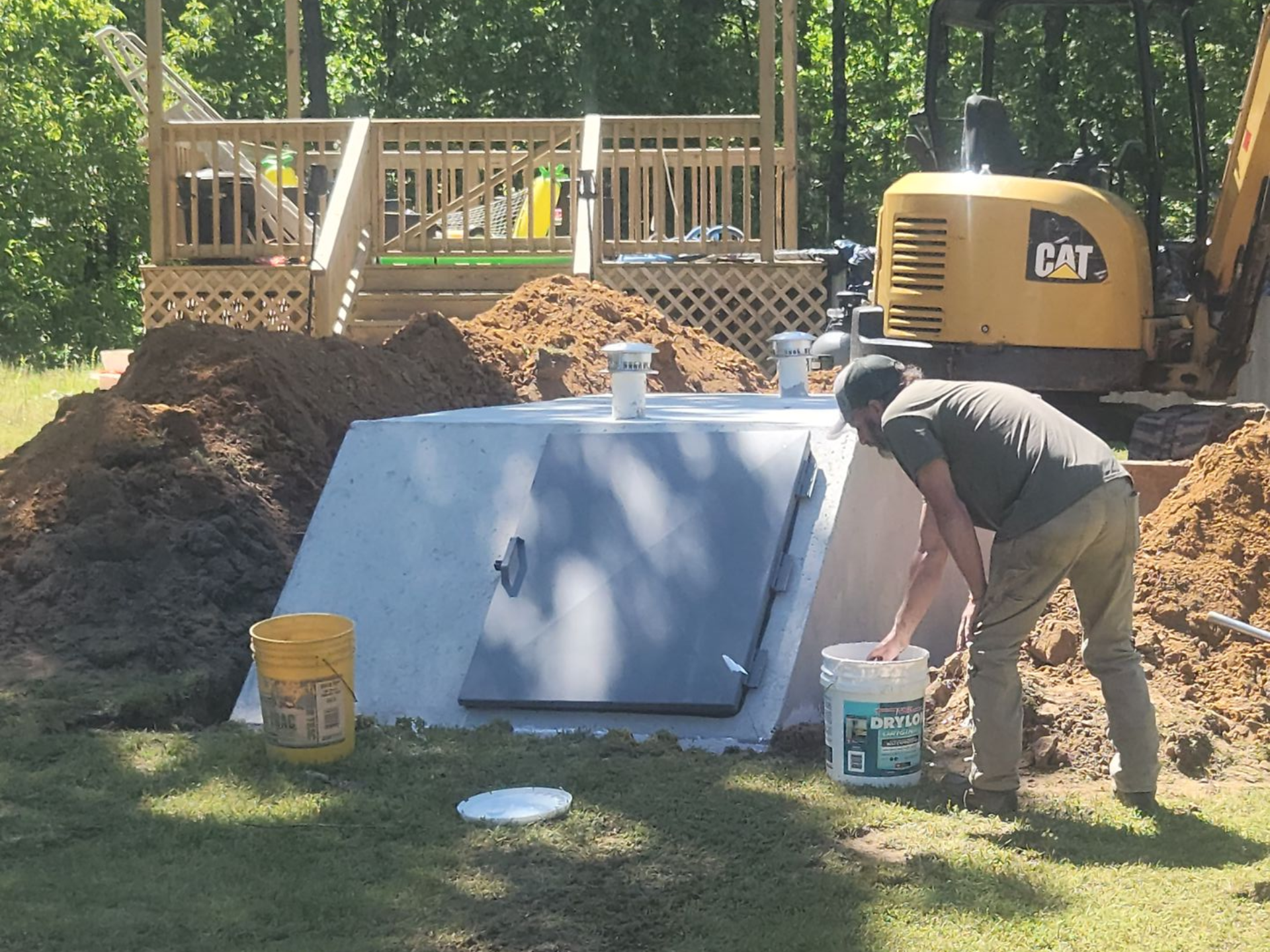 Man preparing a concrete bunker for installation near a deck, excavator in background.