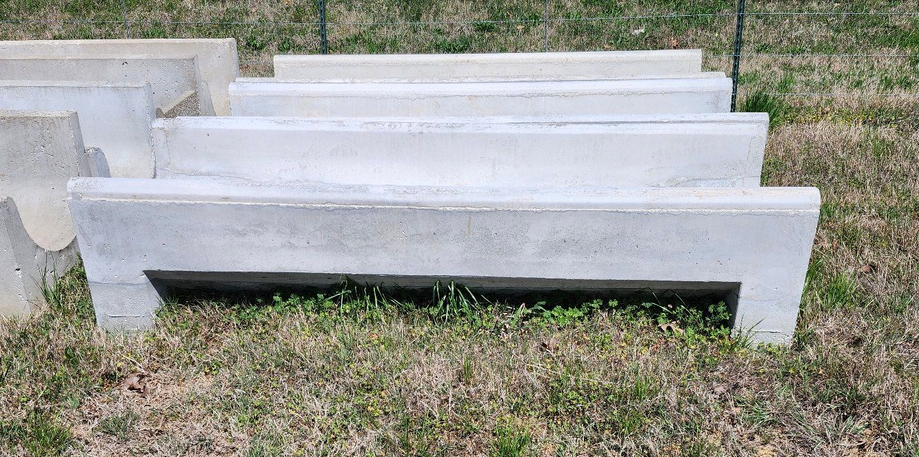 A set of concrete livestock feed troughs arranged in a grassy field.