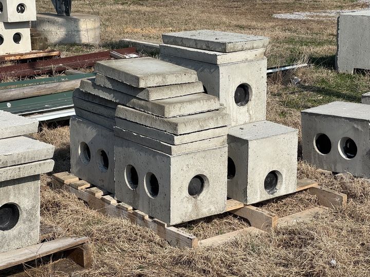 Concrete storm drain catch basins and lids stacked on wooden pallets in an outdoor storage yard.