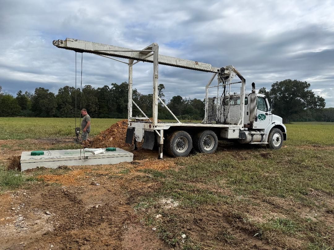 Truck with crane, lifting a large concrete box in a field with a person operating the equipment.